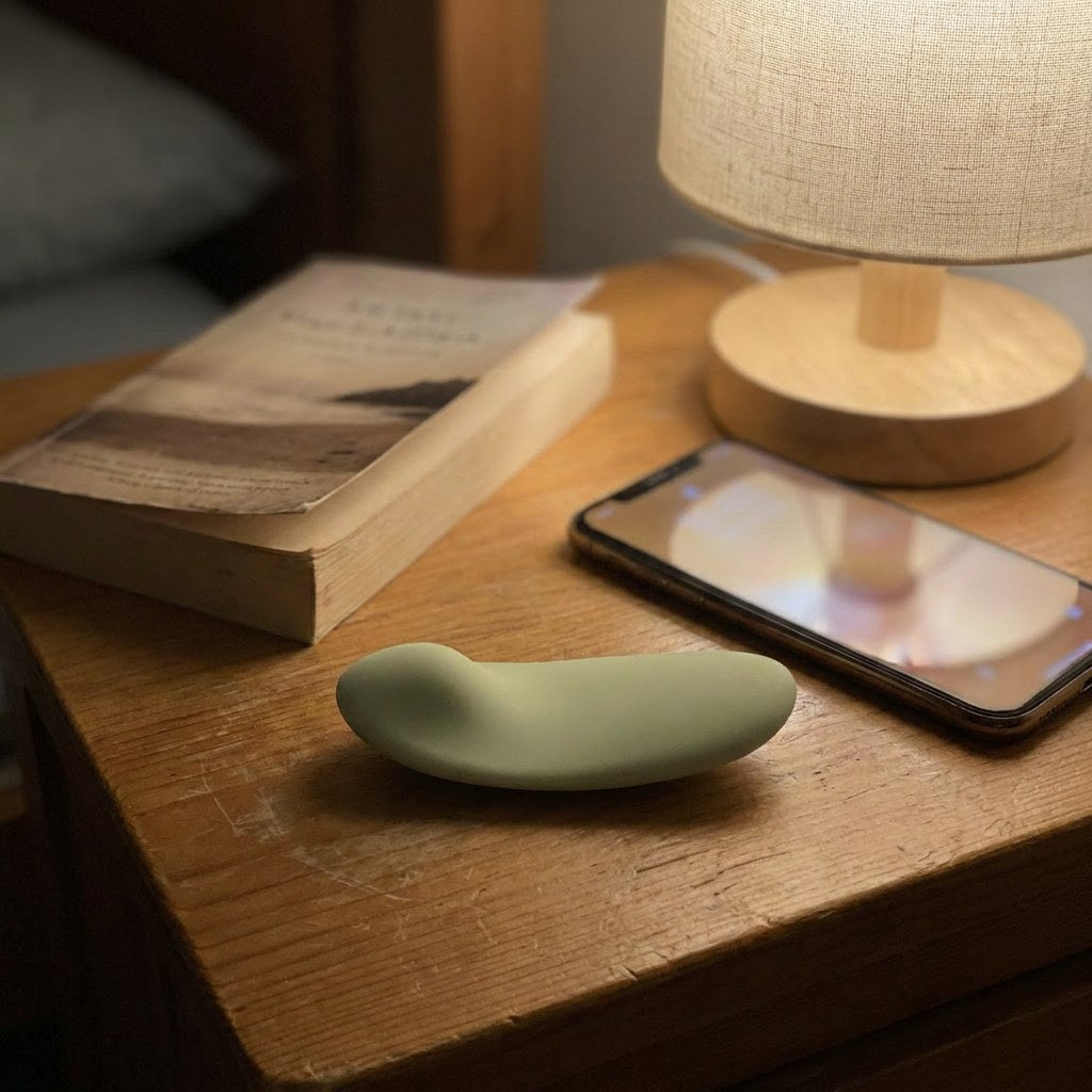 Petal Nyx on a warm wooden nightstand at night beside a book, phone, and lamp — calm and premium